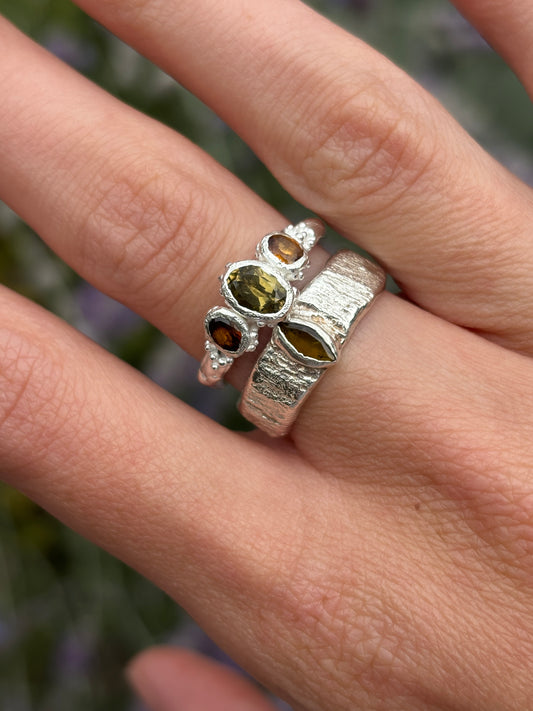 A brown tourmaline fairy ring in sterling silver worn on a hand with a woodland background 