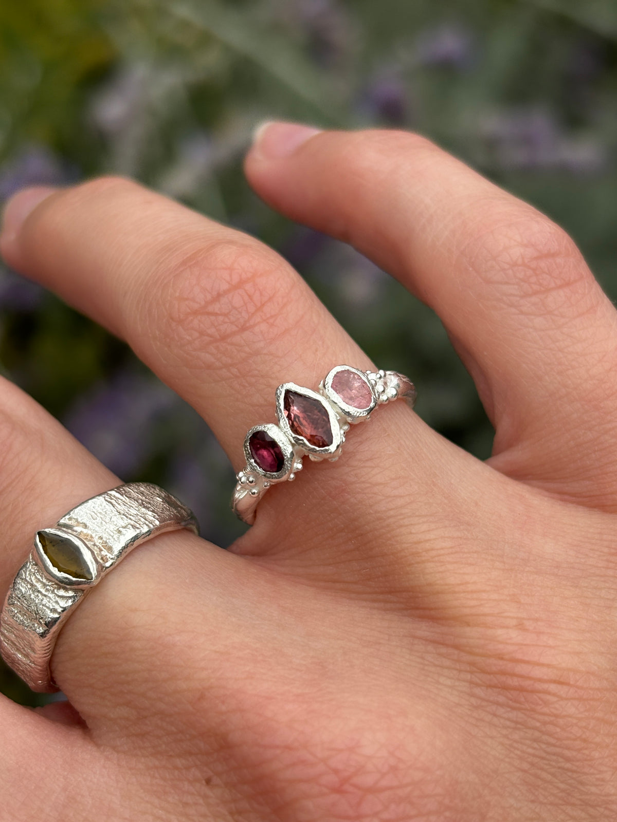 A pink tourmaline fairy inspired ring worn on a hand with a woodland background 